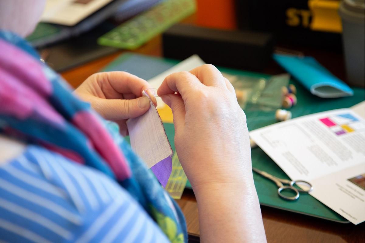 We are looking over someone's shoulder at their hands as they sew together small pieces of silks into a patchwork.