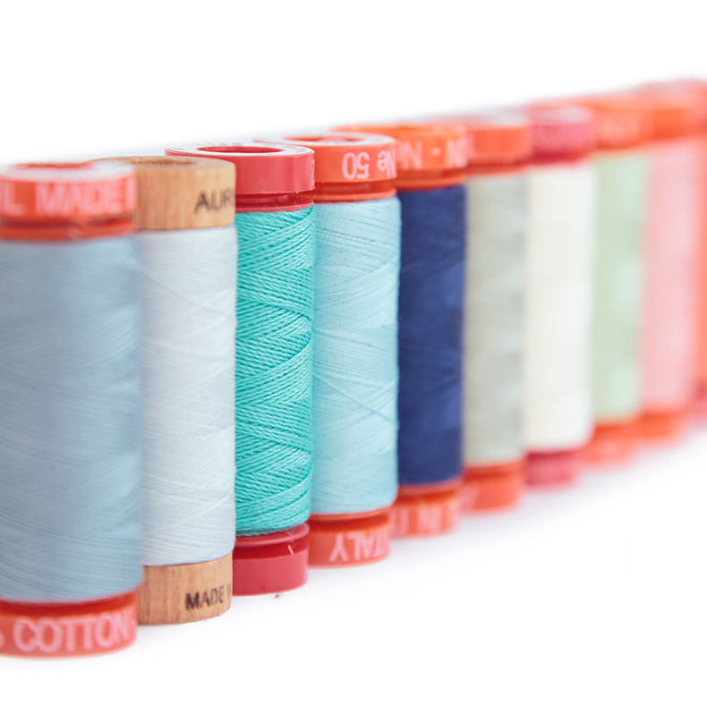 A variety of brightly coloured threads on spools are shown standing on end in a line moving further away from the camera.