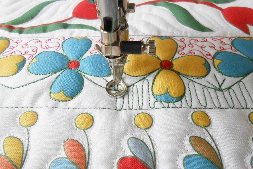 A sewing machine with a free motion foot is stitching a pattern on a colourful floral sample, we cannot see the operator.