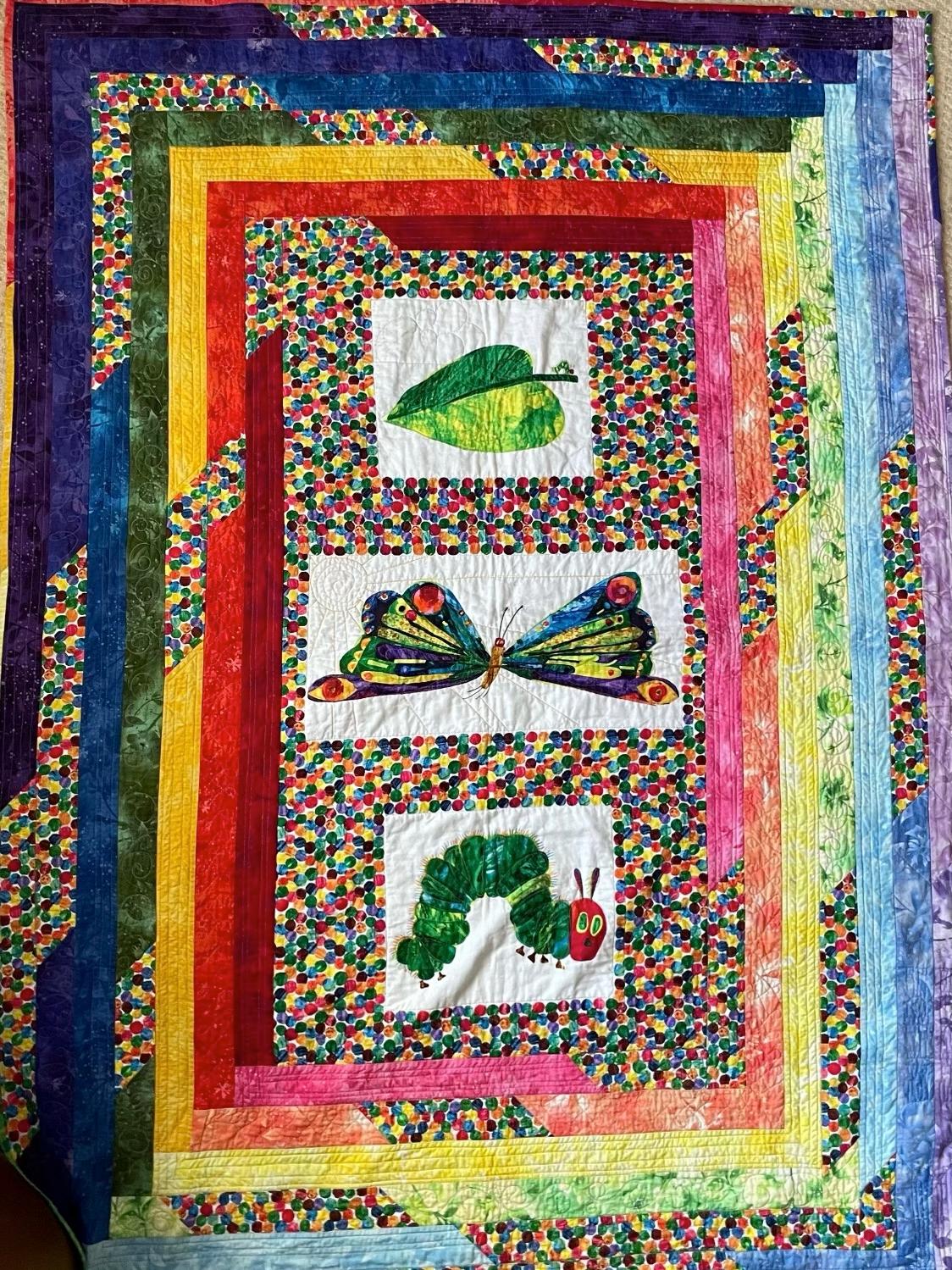 A frame quilt in primary and secondary bright colours, featuring images of a leaf, a caterpillar and a butterfly.