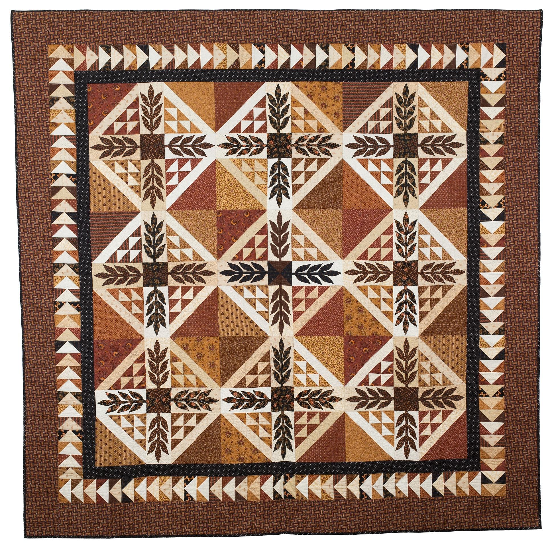 A quilt in earthy tones featuring flying geese blocks and leaf motifs.