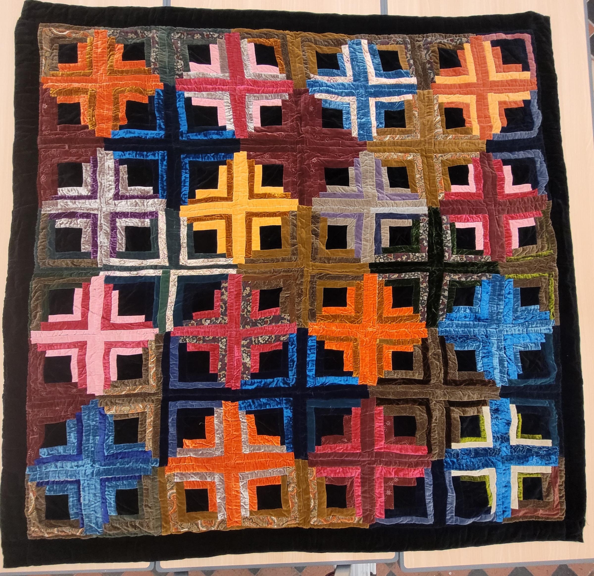Image shows a bright velvet patchwork of log cabin blocks in the 'sunshine and shadow' layout. Browns, blues, oranges, reds and yellows feature prominently.