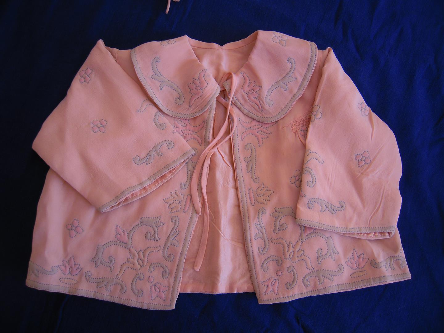 Image shows a milkshake pink 1930s baby's jacket decorated with shadow quilting.