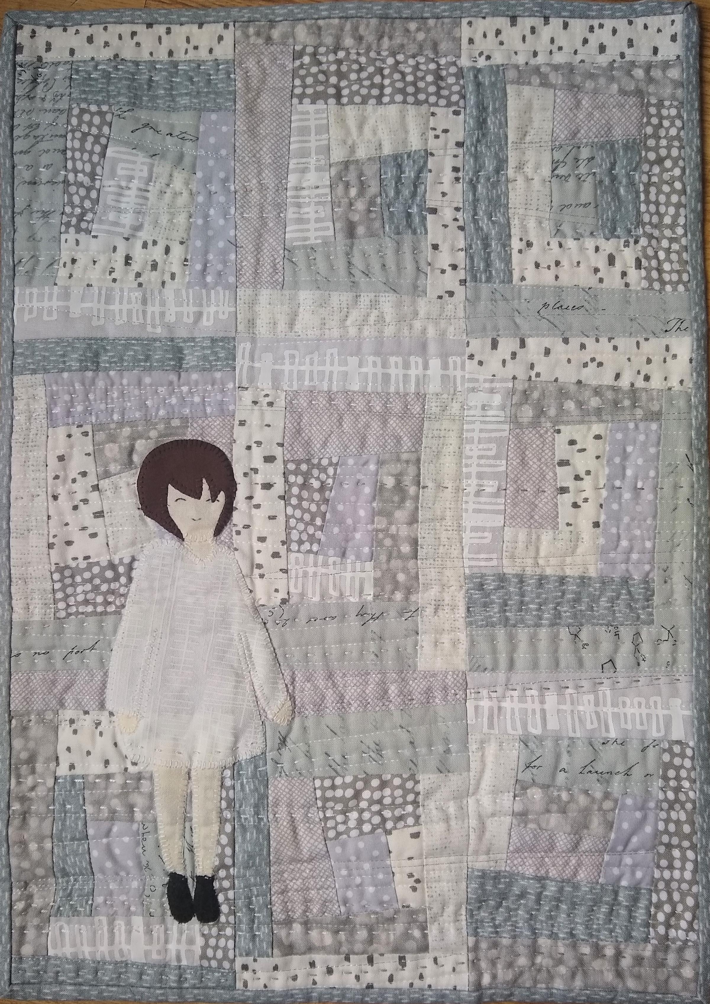 Improv log cabin style quilt in neutrals with an appliqued female figure in a white dress at the bottom left.