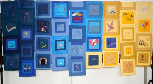 Image shows a quilt made up of many individually hand embellished blocks in blue and yellow.
