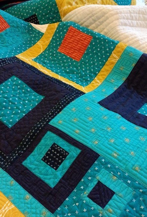 Image shows a close up of an improv blocked quilt in turquoise, blue, orange white and yellow.