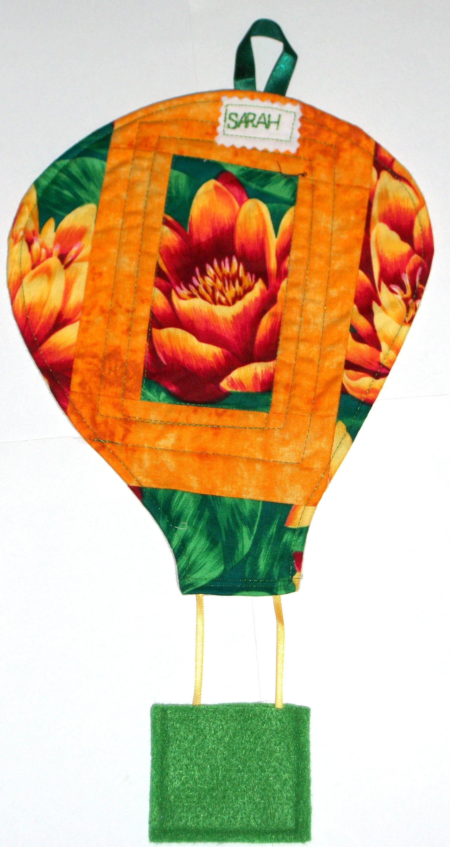 Image shows a quilted hot air balloon in orange and green fabric, with the name Sarah stitched at the top.