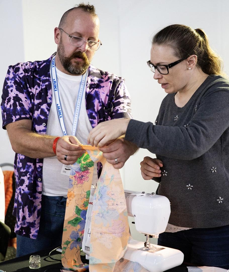 Image shows a white man and woman looking at a fabric project together whilst stood at a sewing machine.