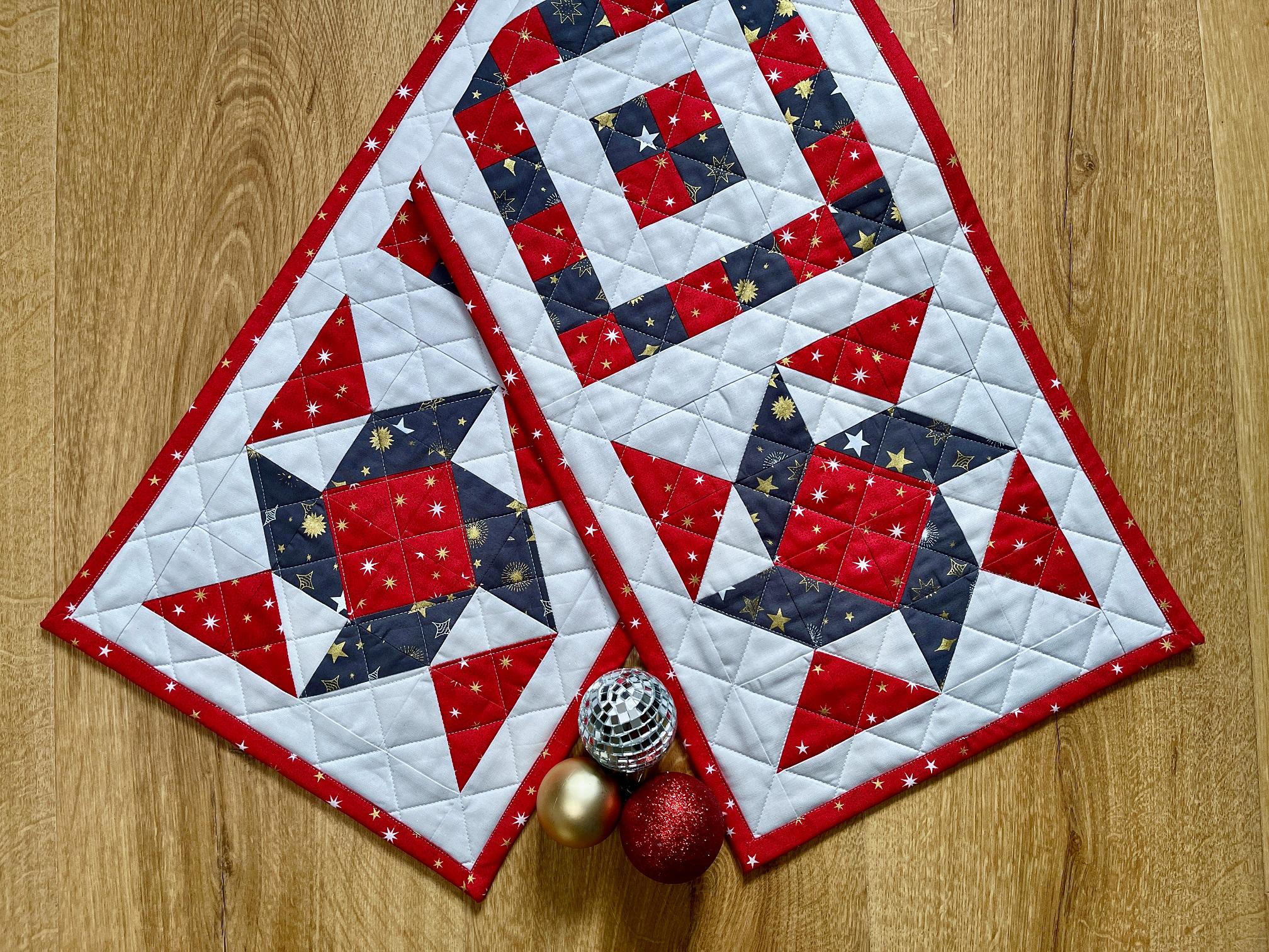Image shows a Christmas patchwork table runner in red, blue and white, with some baubles nearby