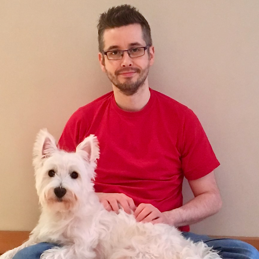 A man in a red t-shirt with short brown hair, a short beard and glasses, sits with a West Highland Terrier in his lap