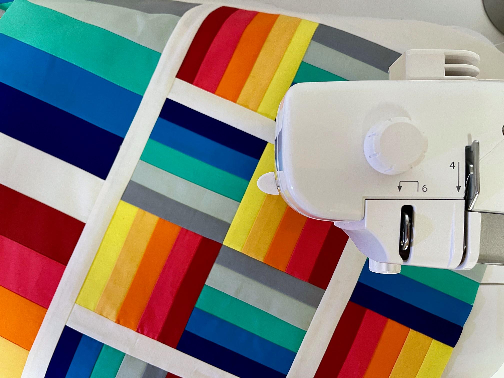 A quilt top made of strip pieced quartered squares in alternately warm and cool shades rests in the bed of a sewing machine