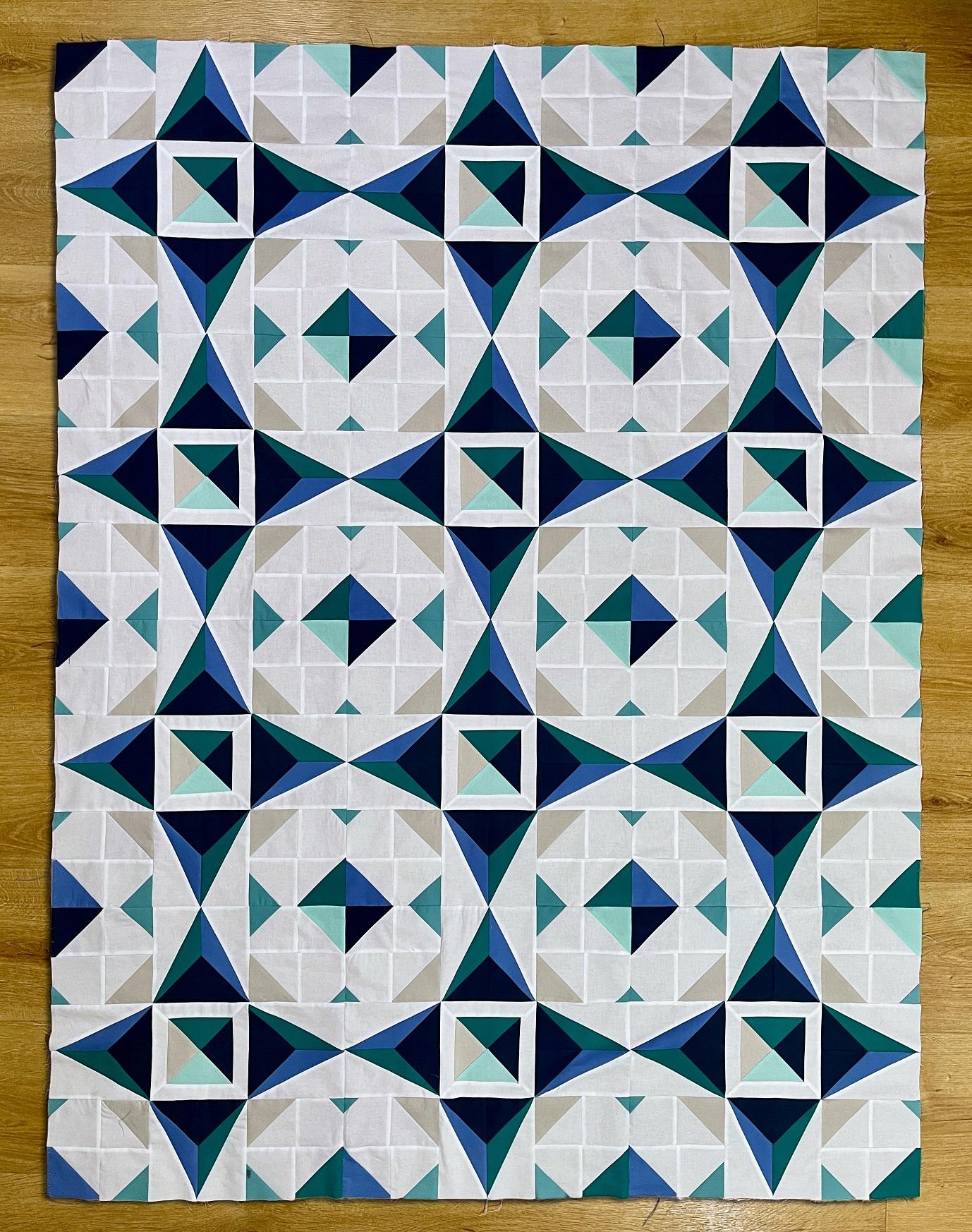 Image shows a patchwork quilt top pieced to look like repeating faceted diamonds in shades of blue, green and pale greys