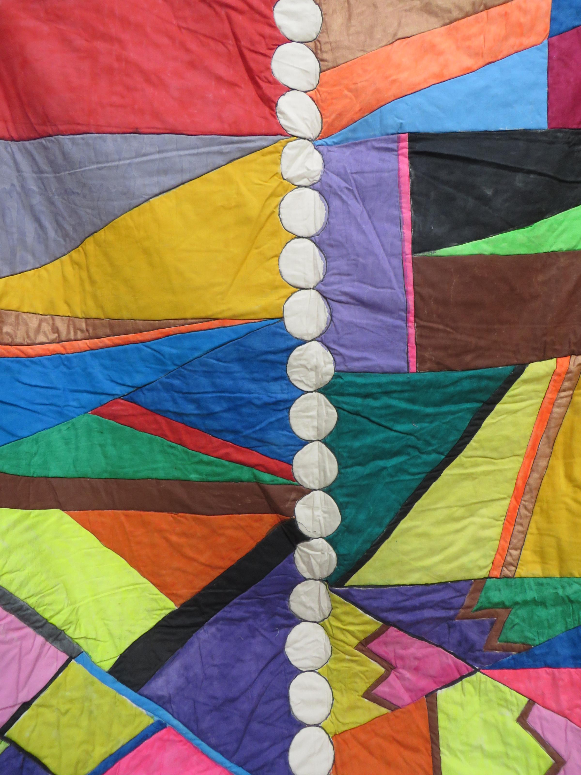 A quilt featuring random geometric shapes in bright colours with a line of white circles down the centre