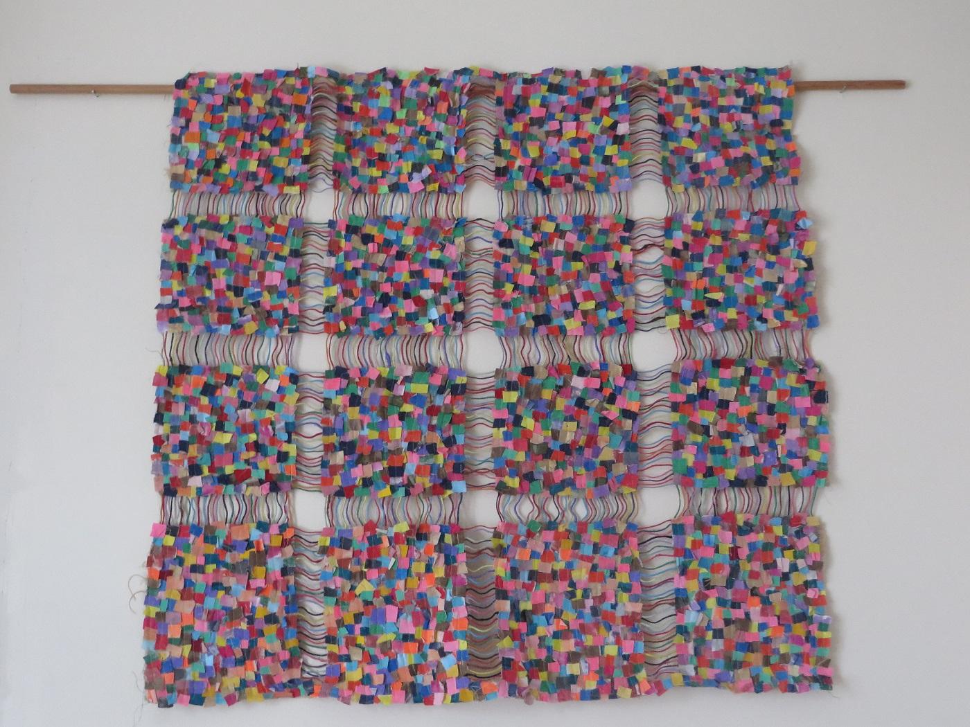 A brightly multi-coloured wall hanging made of tiny squares of fabric.