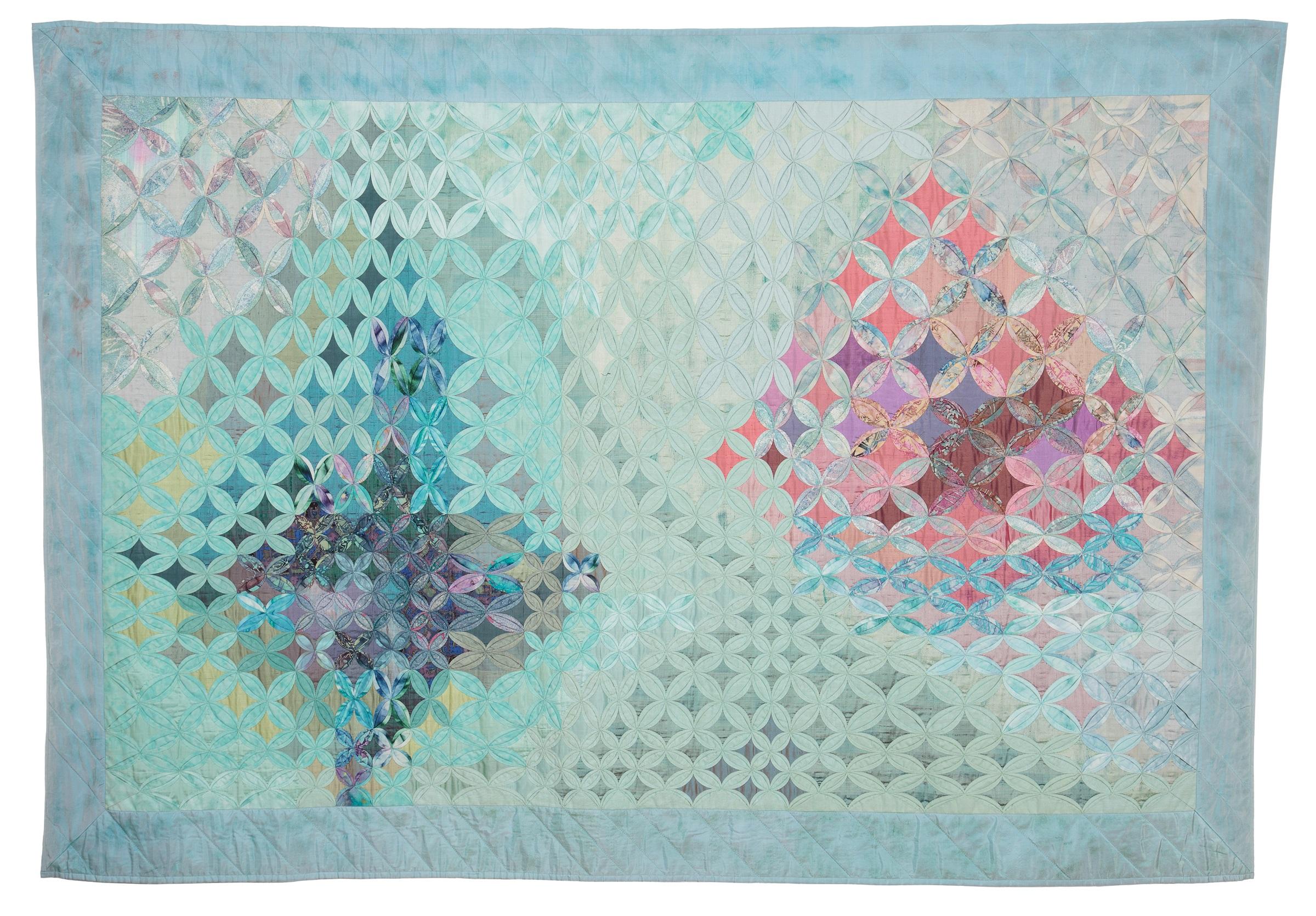 A landscape-format cathedral windows quilt in purples, blues, turquoises and pinks.