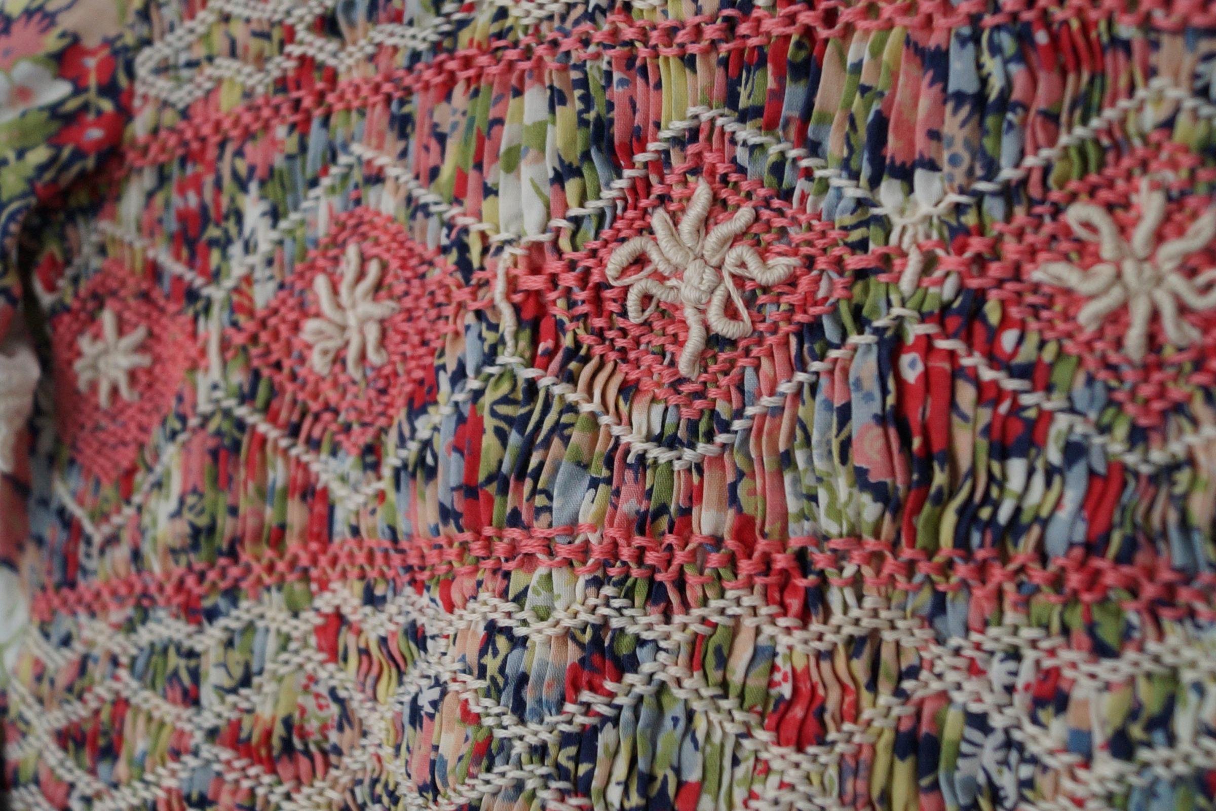 Close up image of a smocked dress for a young girl in liberty fabric with red and white smocking stitches.