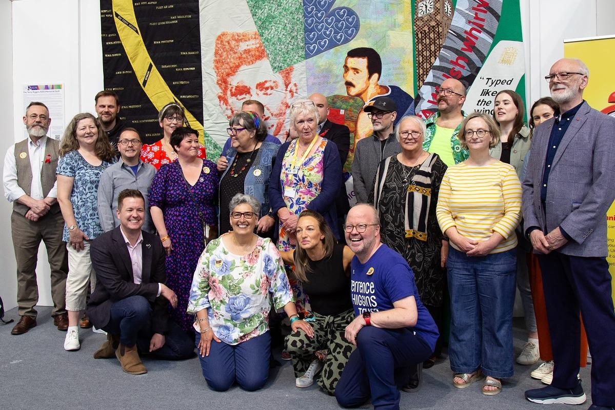 A group of people who were involved in making the quilt stand in front of the Terry Higgins Memorial Quilt