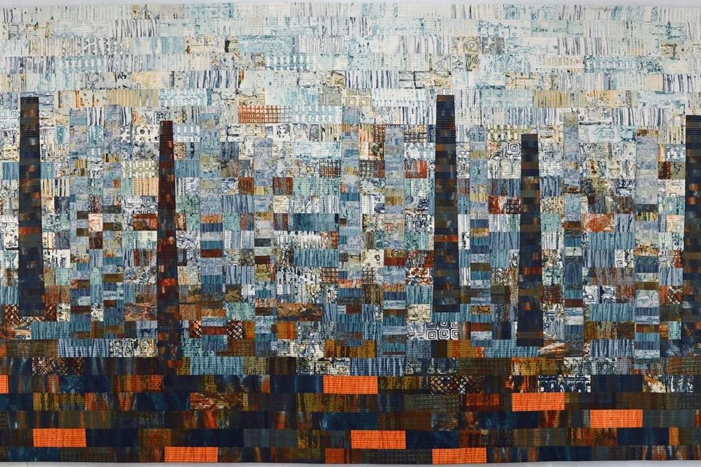 A patchwork quilt in shades of blue and orange depicting an industrial chimney-scape.