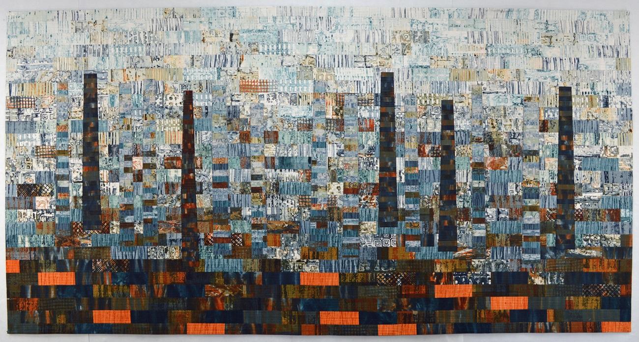 A patchwork quilt in shades of blue and orange depicting an industrial chimney-scape.