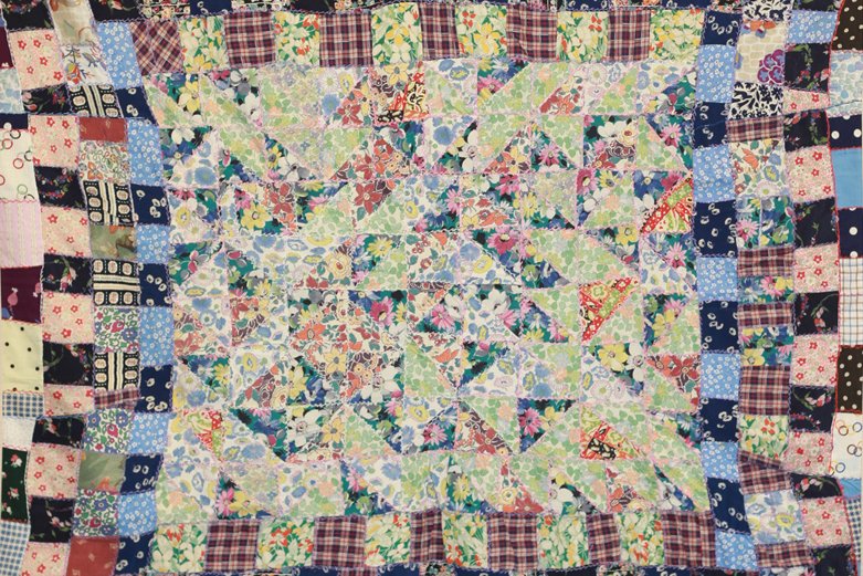 Wartime patchwork coverlet made from multicoloured fabric squares and triangles with embroidered seams and a central geometric design