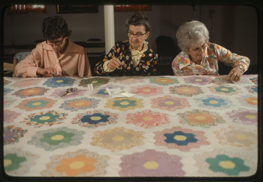 Eva Philips, Lora King and Crystal Cruise sit at a quilt frame 1978