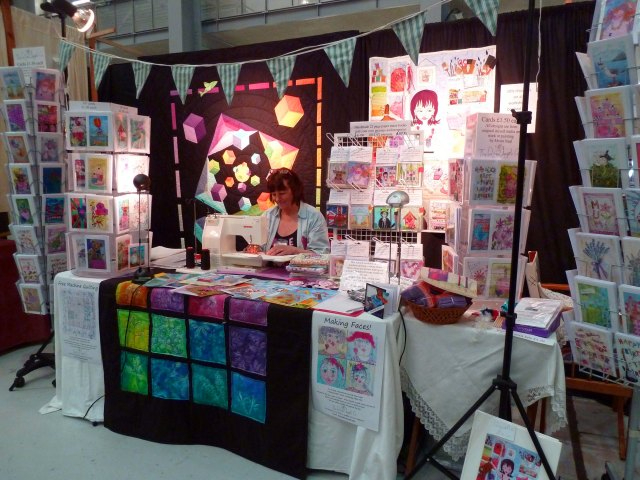 Woman working on sewing machine at a festival stall with quilts and greeting cards on display