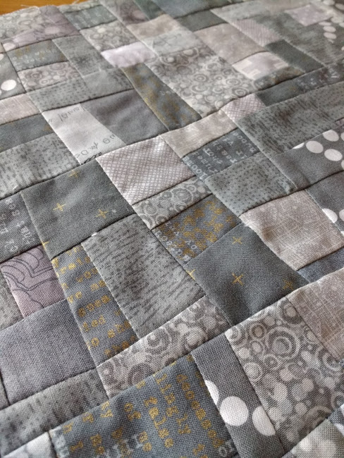 Close up of quilt made of square and rectangles in different grey patterned fabrics