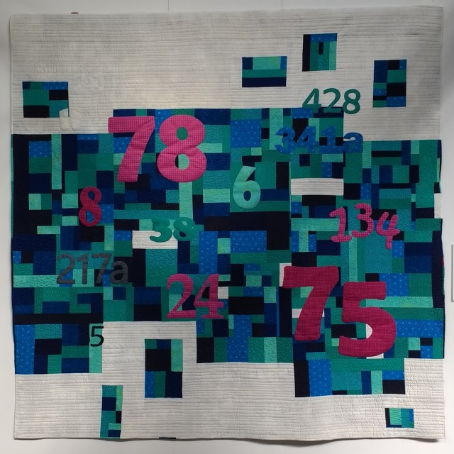 Not Just A Number by Sarah Humphreys: Quilt with beige background and pattern of blue and green squares layered with pink and green numbers