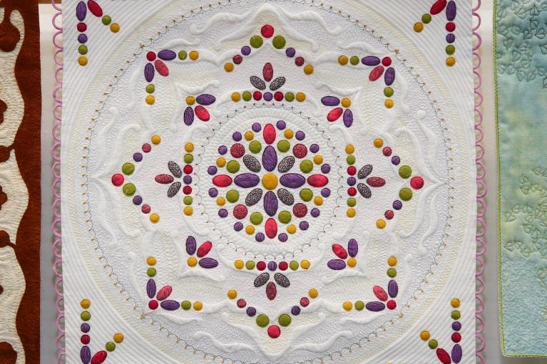 Miniature quilt with white background and a multicoloured design made of small circles and ovals inside a central circle 