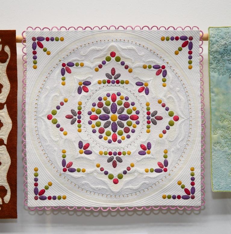Miniature quilt with white background and a multicoloured design made of small circles and ovals inside a central circle