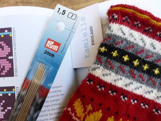 A book open on a double page spread with some knitting and knitting needles on top