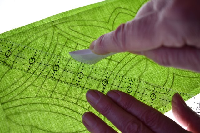 Hands holding a craft knife and ruler cutting a piece of green fabric