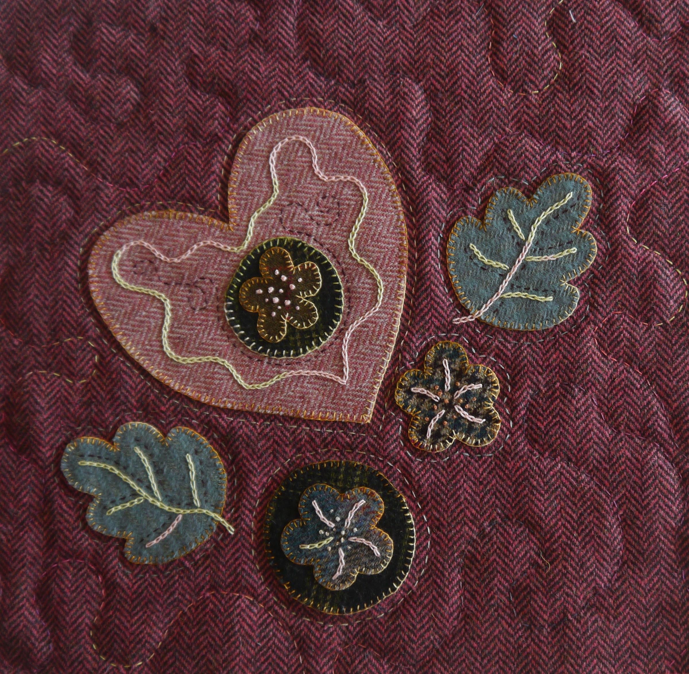 Appliqué work on burgundy herringbone tweed woollen fabric depicting hearts, leaves and flowers