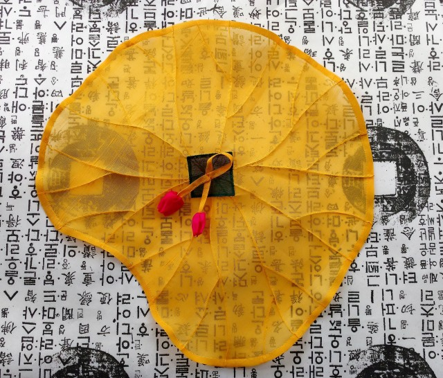 Lotus Flower covering cloth, 2016, by Sara Cook: yellow organza flower shaped cloth on a background of korean letters.