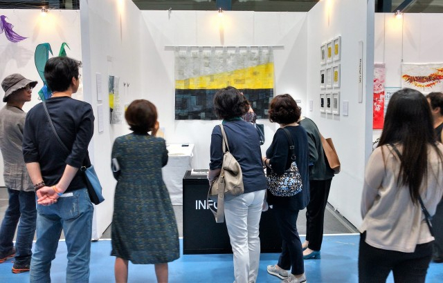 Group of people standing looking at quilts on display at an exhibition