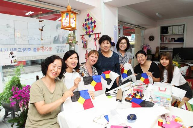 Group of ladies sat around a table in the middle of a classroom holding up their work