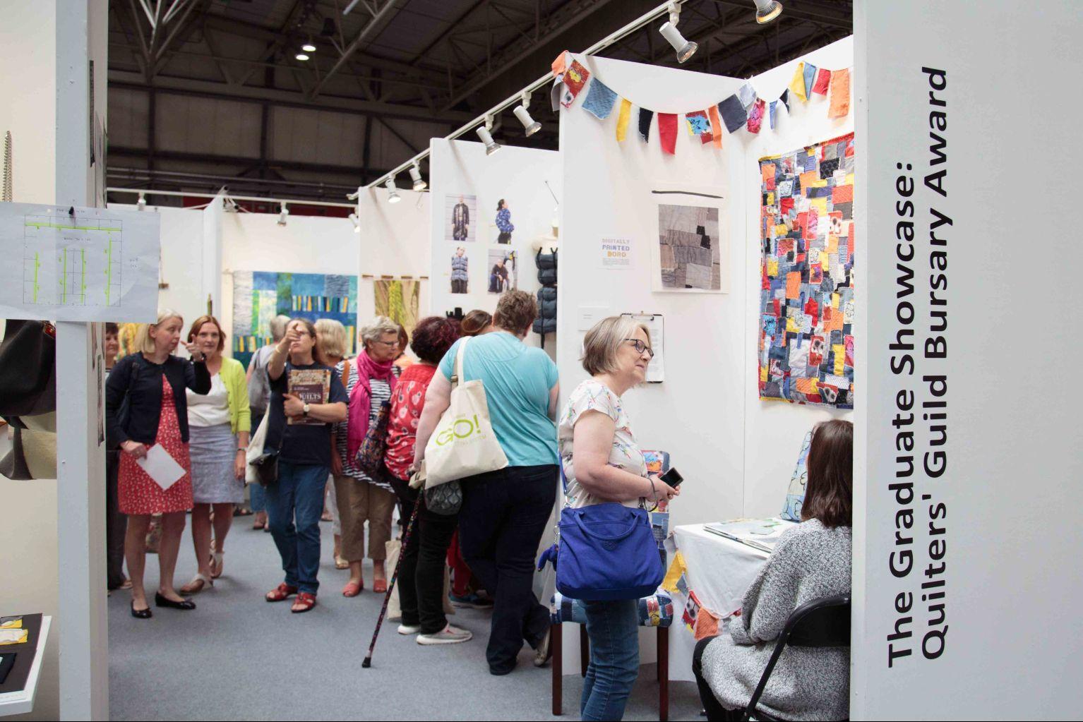 People visiting The Graduate Showcase: Quilters' Guild Bursary Award stand at the Festival of Quilts