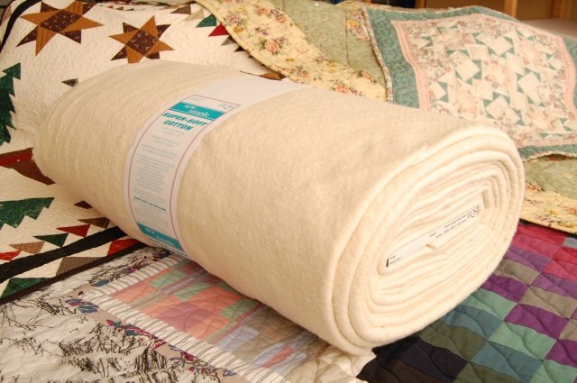 Roll of super-soft cotton wadding laid on a collection of patchwork quilts