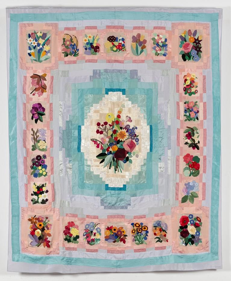 Quilt in turquoise and pinks with a central pieced bouquet of flowers surrounded by squares of different flower groups. 