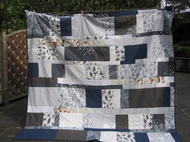 Large quilt made of squares and rectangles in navy, grey, neutral and liberty print fabrics with organza flowers stiched in.