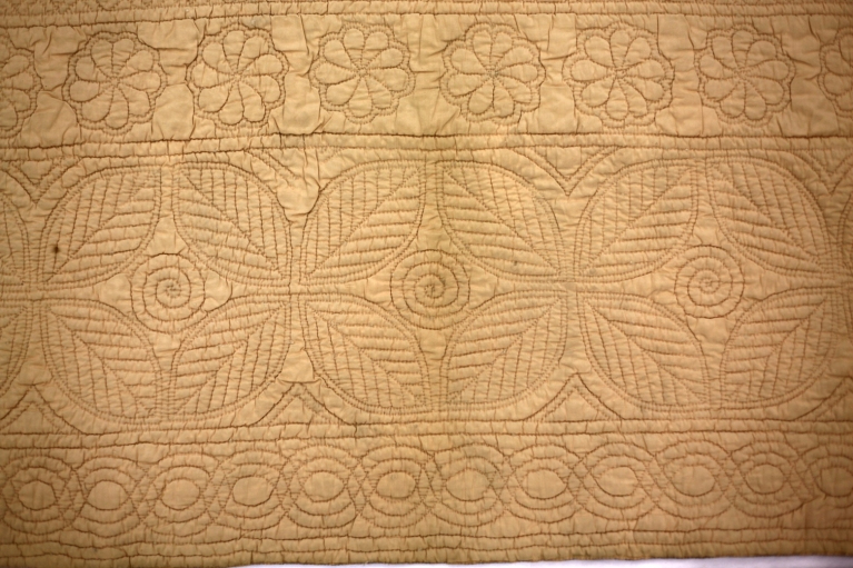 Peach coloured wholecoth quilt reversing to blue, quilted in a classic Welsh centre and defined borders layout, with typical Welsh motifs.