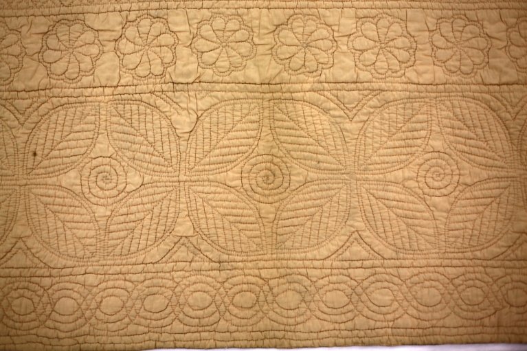 Peach coloured wholecoth quilt reversing to blue, quilted in a classic Welsh centre and defined borders layout, with typical Welsh motifs.