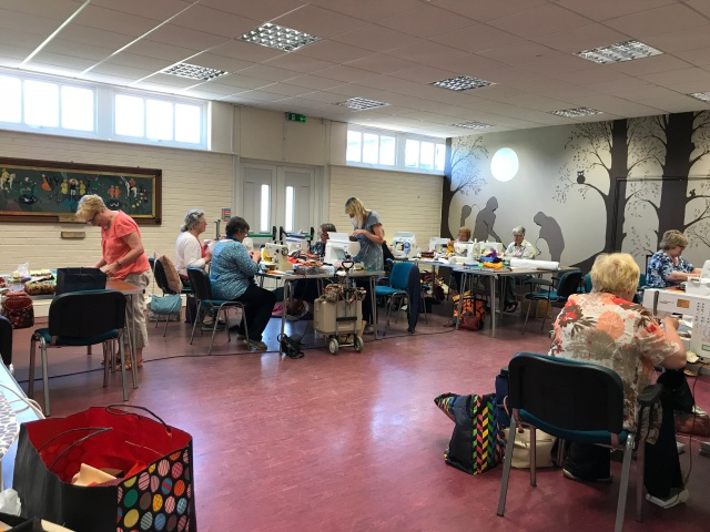 Ladies sat at tables in a hall, sewing with sewing machines