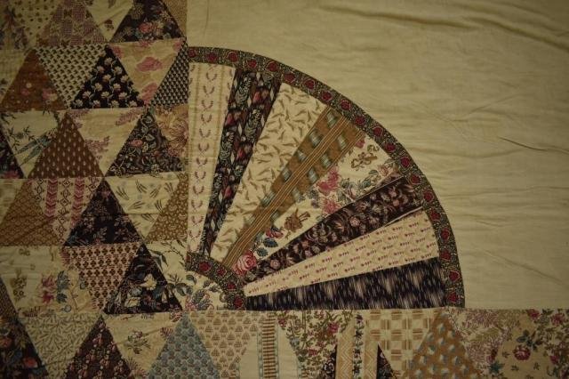 Close up of the corner of a patchwork quilt showing a fan pattern made of different fabrics