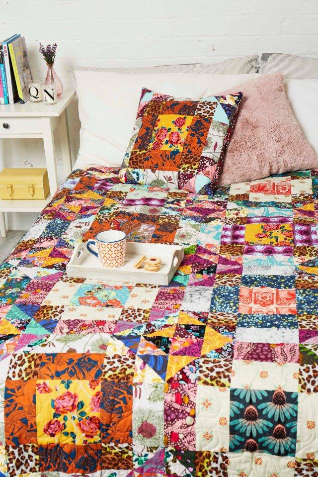 A tray with a mug and biscuits on, on a bed with vibrant multi-coloured patchwork bedding