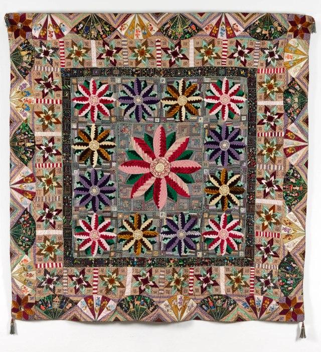 The Jubilee Quilt, c.1887. Quilt made of many different shaped pieces, in many different fabrics, creating flower and fan shapes around a central square