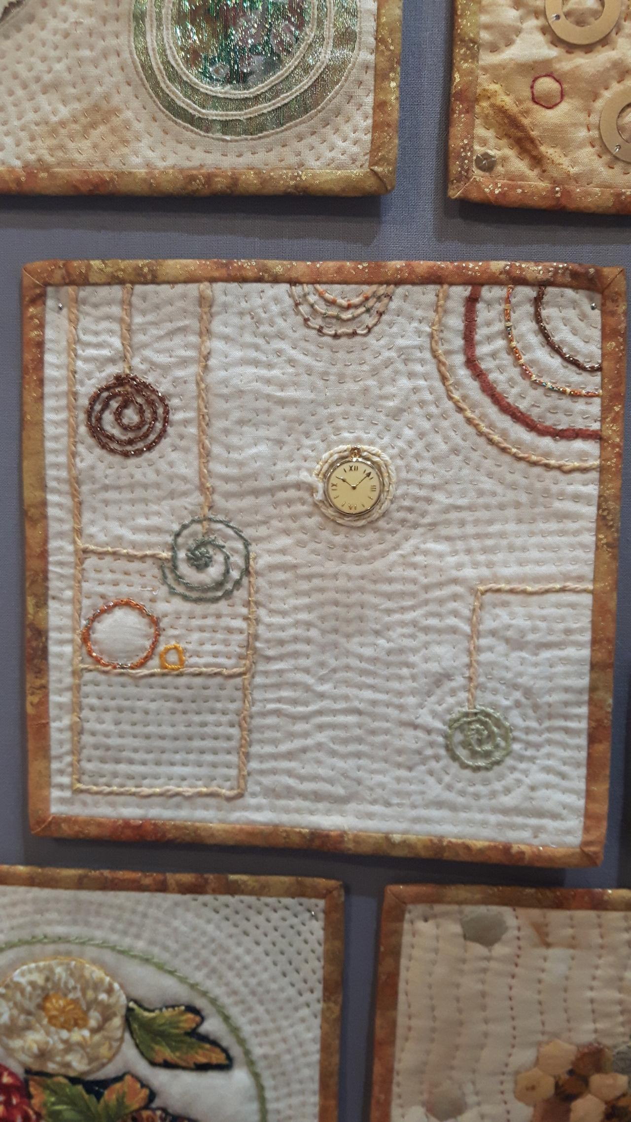 Display of cream and gold miniature quilts on a wall