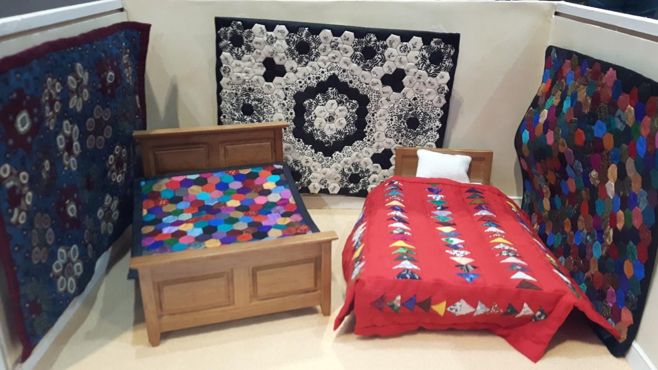 Display of 5 miniature quilts, 2 displayed on doll's house beds