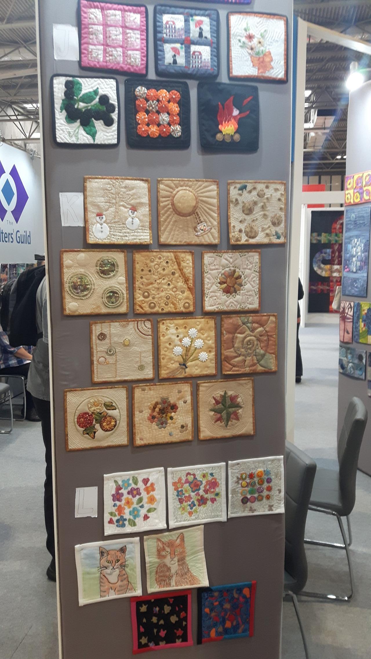 Multiple square miniature quilts on a display board at an exhibition