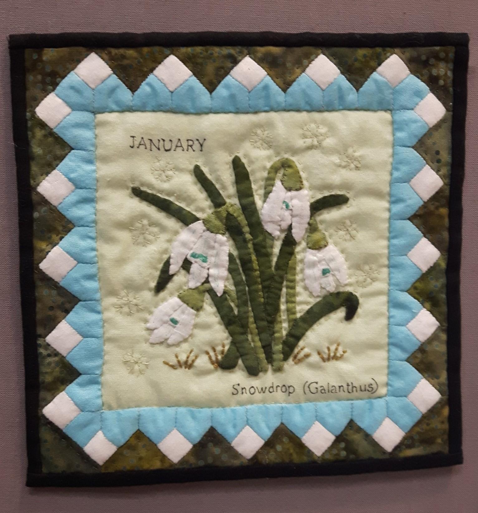 Miniature quilt depicting snowdrops growing on a cream background with a blue and white border